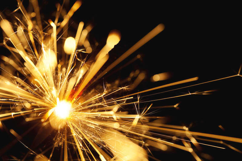 Close-up of a lit sparkler throwing golden sparks against a dark background