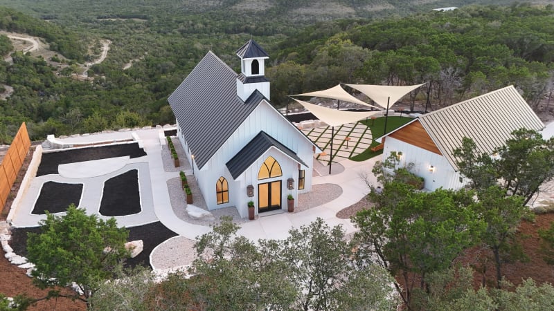 Aerial view of The Chapel at Wimberley and its gathering courtyard on a Hill Country hilltop, surrounded by miles of green cedar and oak